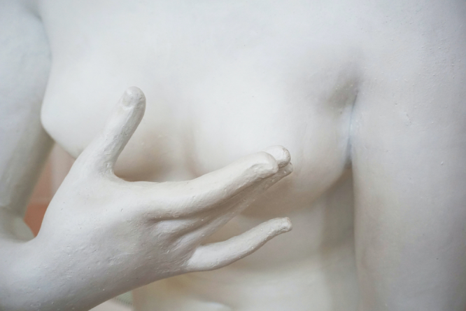 Pic of a nude body made of white clay with a right hand 3rd finger touching left breast nipple